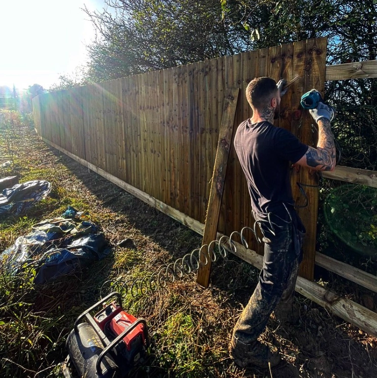 an image of a person fitting fence panels, using a hammer and equipment.