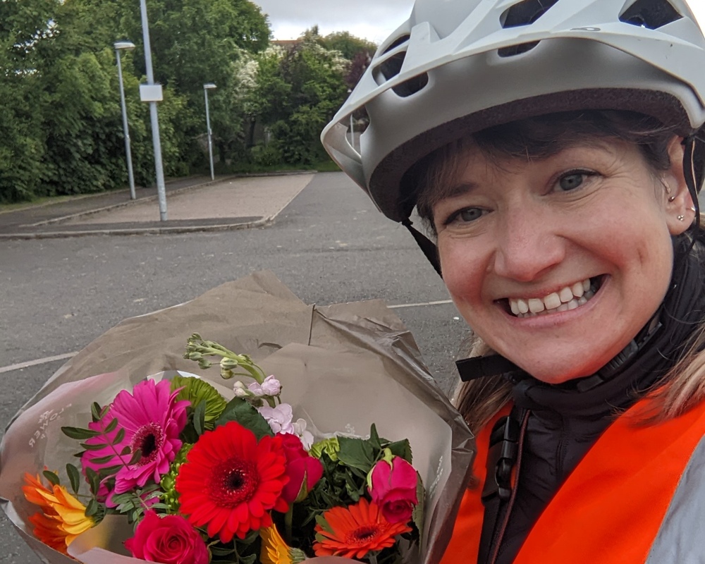 Bikeability volunteer Kirsty wearing a bike helmet and holding flowers