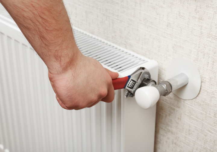 an image of a man using wrench to turn the valve of the radiator