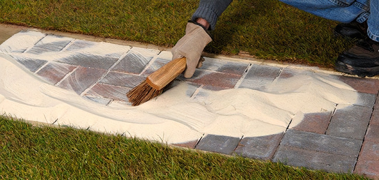 an image of a man applying kiln-dried sand across the block paving