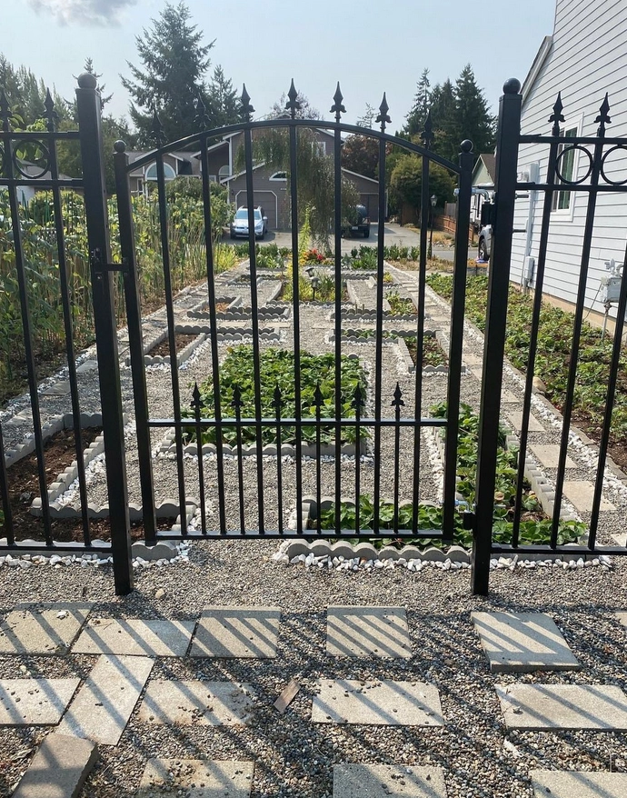 A metal garden gate leading to a graveled area with patio slabs surroudning it. 