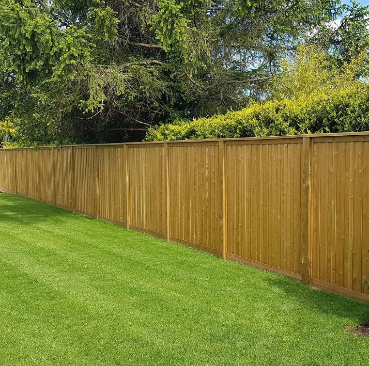 an image of a long, brown coloured fence amongst green grass in a garden.