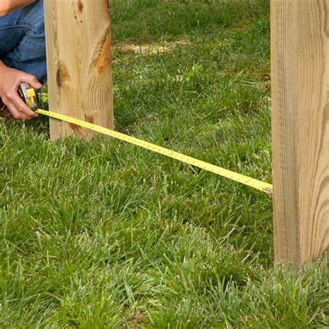 an image of a man measuring the distance between two wooden gate beams