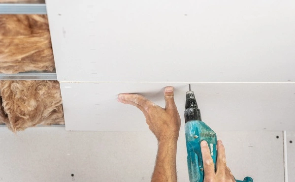Hands using a drill to plaster a ceiling.Insulation also spotted to the side as well.