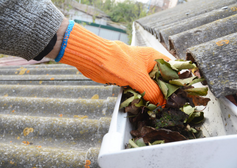 an image of some gutters filled with leaves. A person is removing them