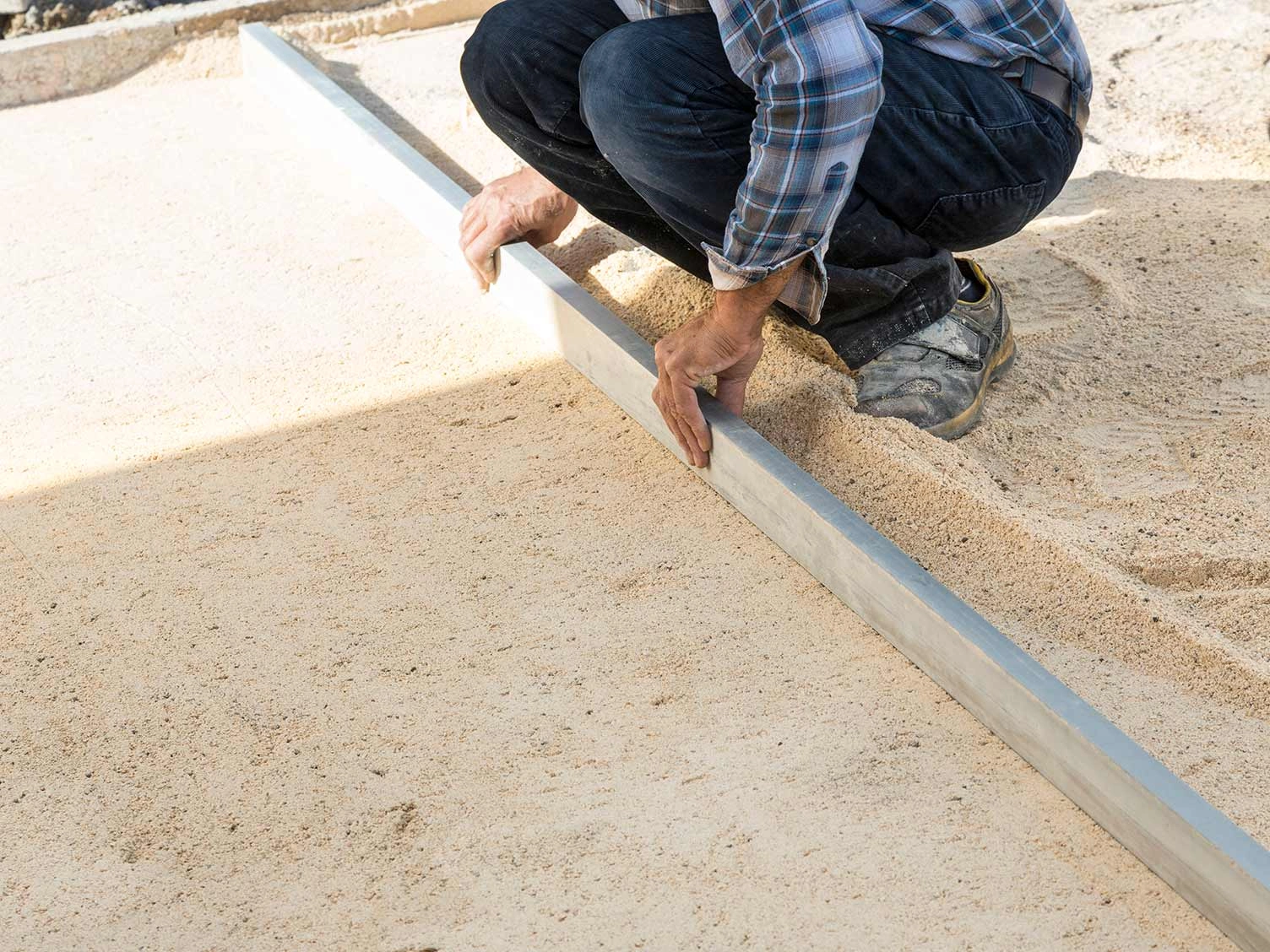 A person using a rake to rake the sand over the sub base to create the pefect foundation for a patio.
