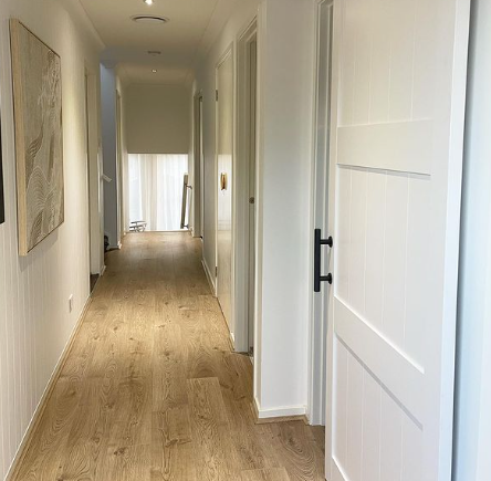 an image of a hallway with white walls and doors and laminate floors