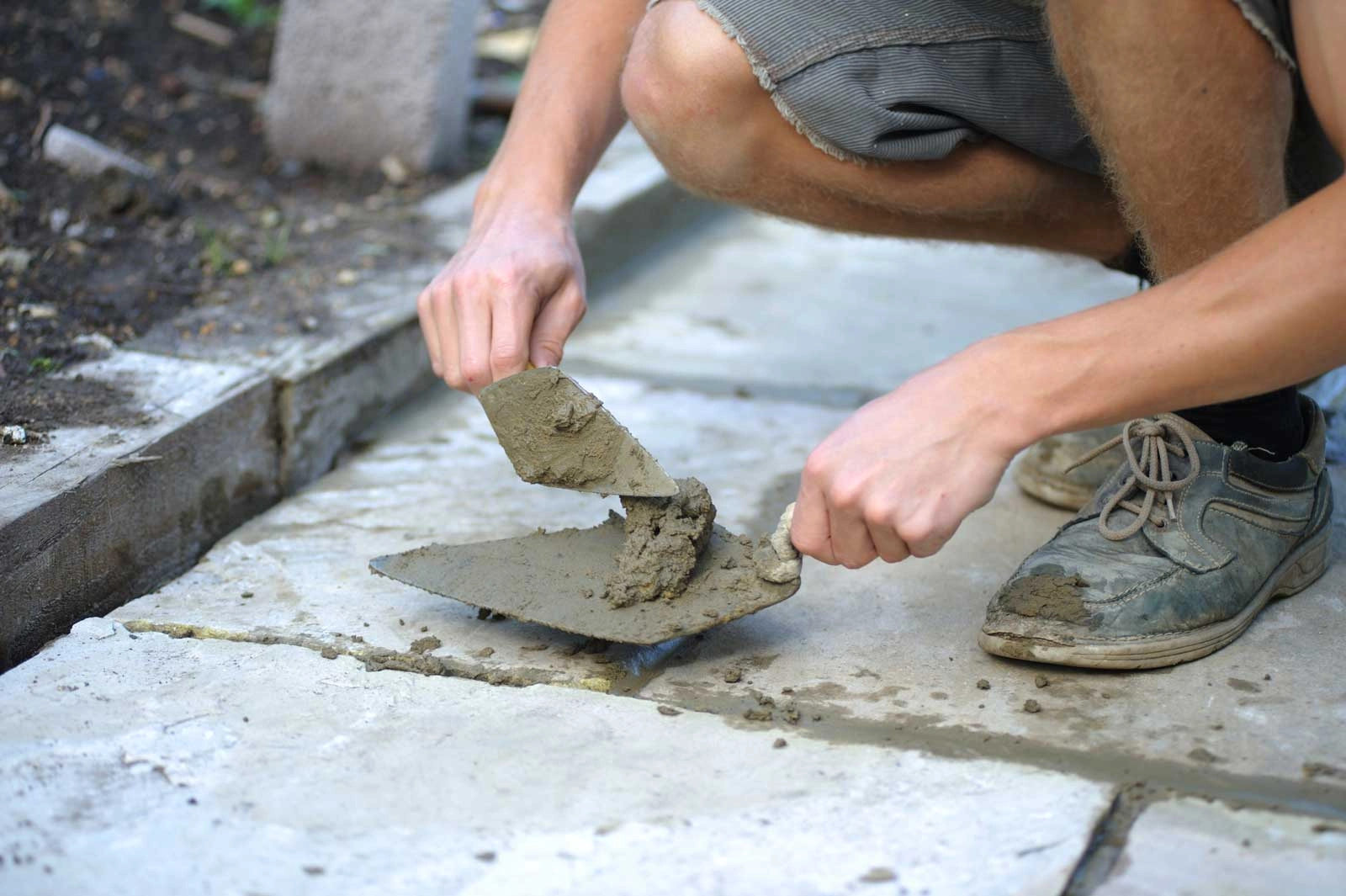 A person using mortar on a spade to join concrete paving slabs together. 