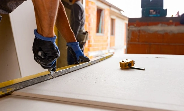 Hands using a stanley knife to cut into plasterboard.