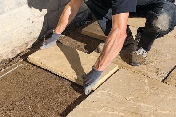 A person laying paving slabs on the top of a sub base to fit a patio.