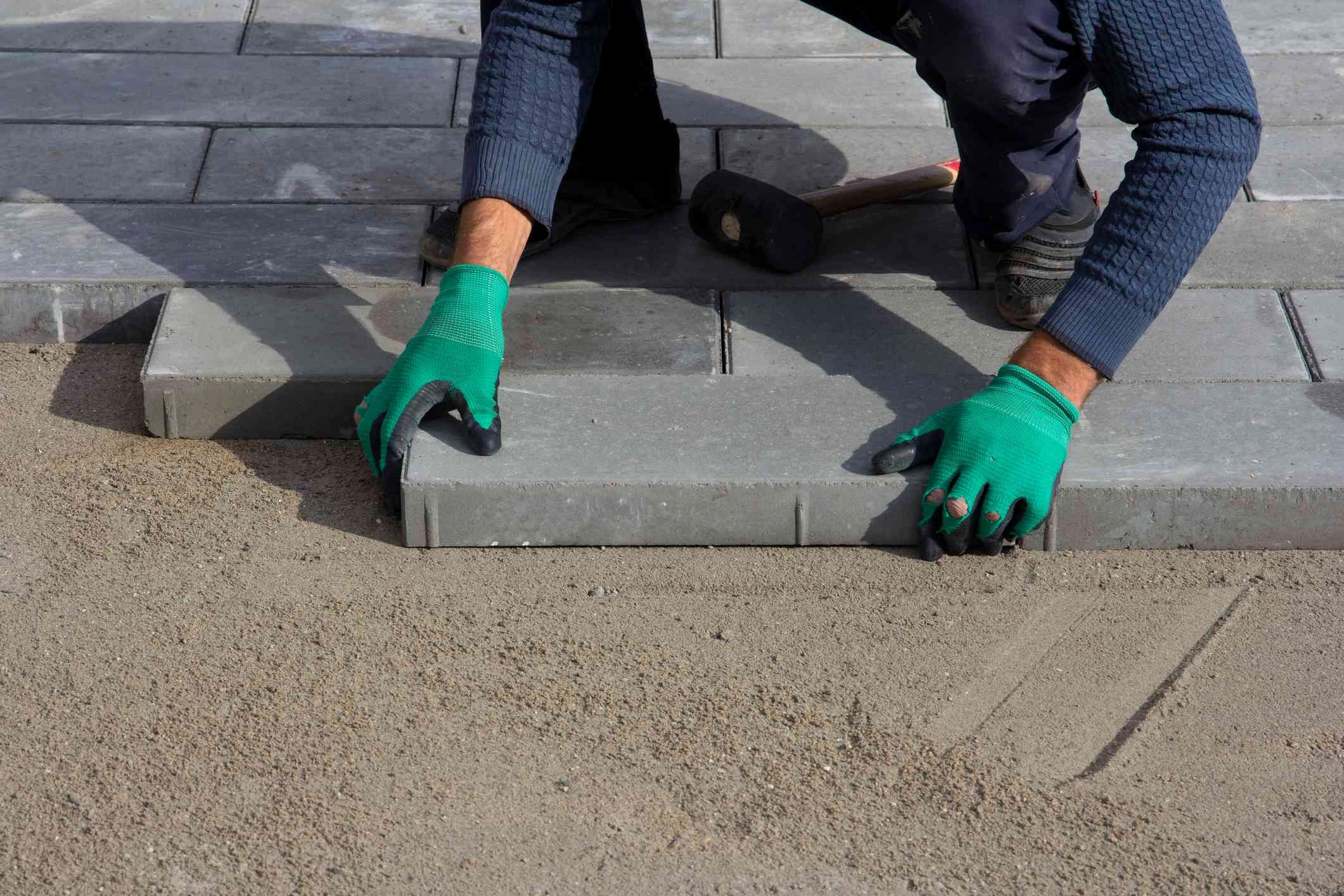 A person wearing safety gloves fitting concrete paving slabs on top of a sub base for a patio.