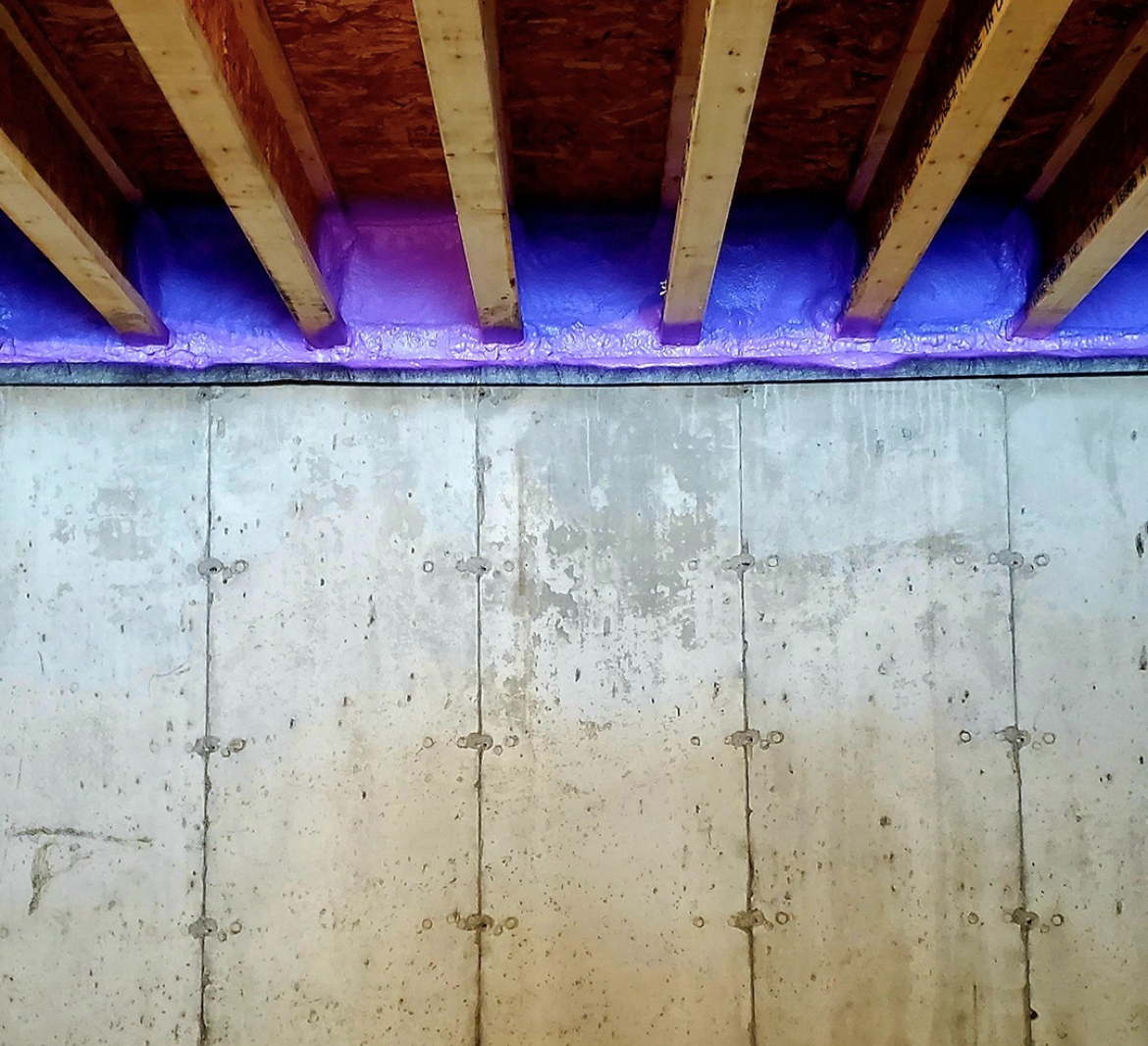 An image showing a wall with wooden beams on the ceiling with insulation installed in the gaps.