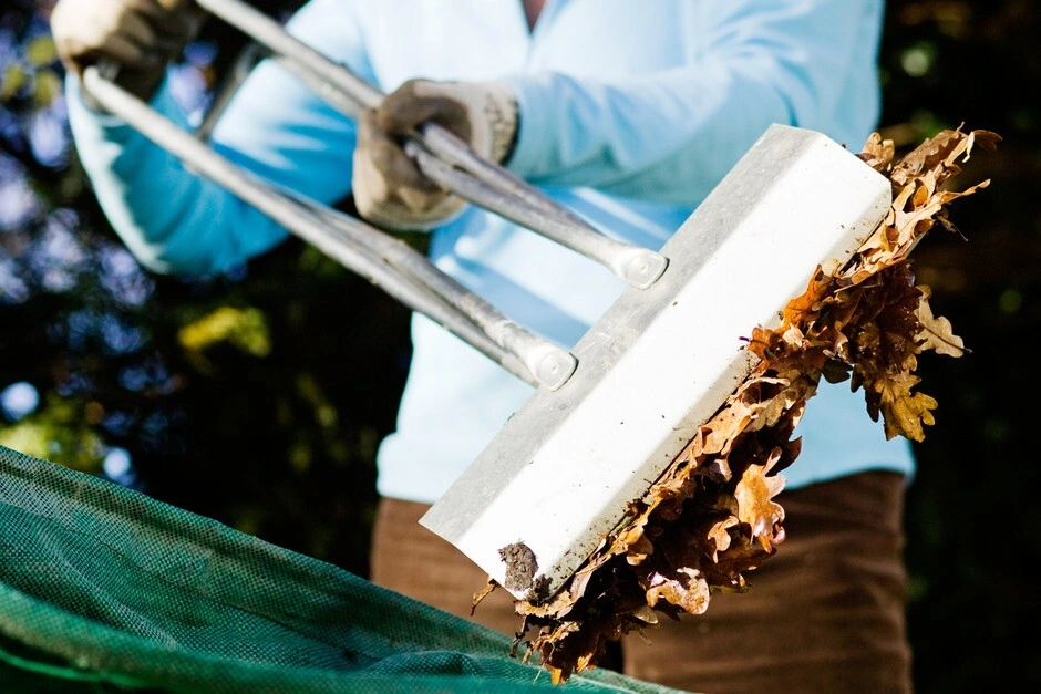 A person using a leaf collector to get rid of any autumn leaves from their garden.