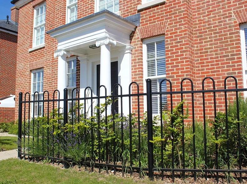 Front Garen fence made of iron wrought bordering someone's front garden with a bricked house behind it.