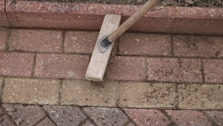 An image of a brown bristle brush being used to effectively clean and maintain block paving by getting rid of oil stains, algae and dirt.