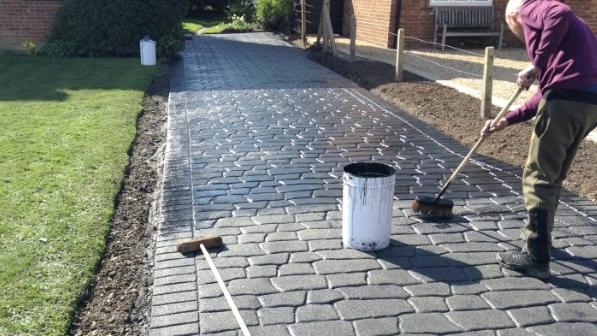 An image of a person using a bristle brush and bucket to successfuly clean their block paving driveway, which is at the front of their house. 