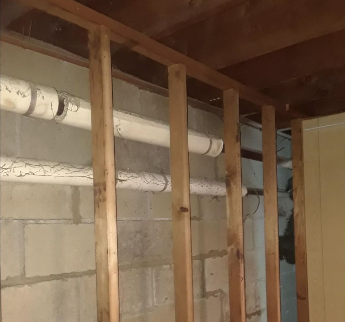 An image showing a wooden stud wall with pipes behind wrapped in pipe insulation. Gaps shown in the insulation and cracks formed.