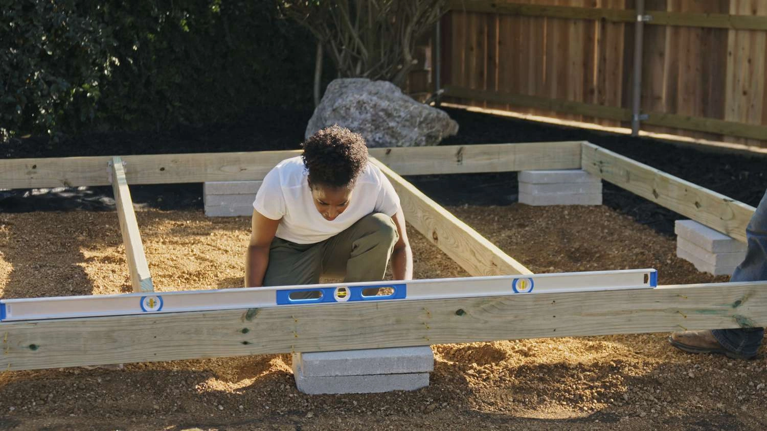 A woman laying a decking sub frame over the soil in the garden and surrounded by joists
