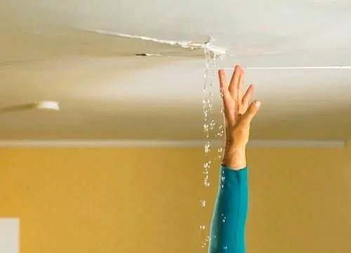A hand reaching up towards a leak in the ceiling, indicating a possible leak in the attic.