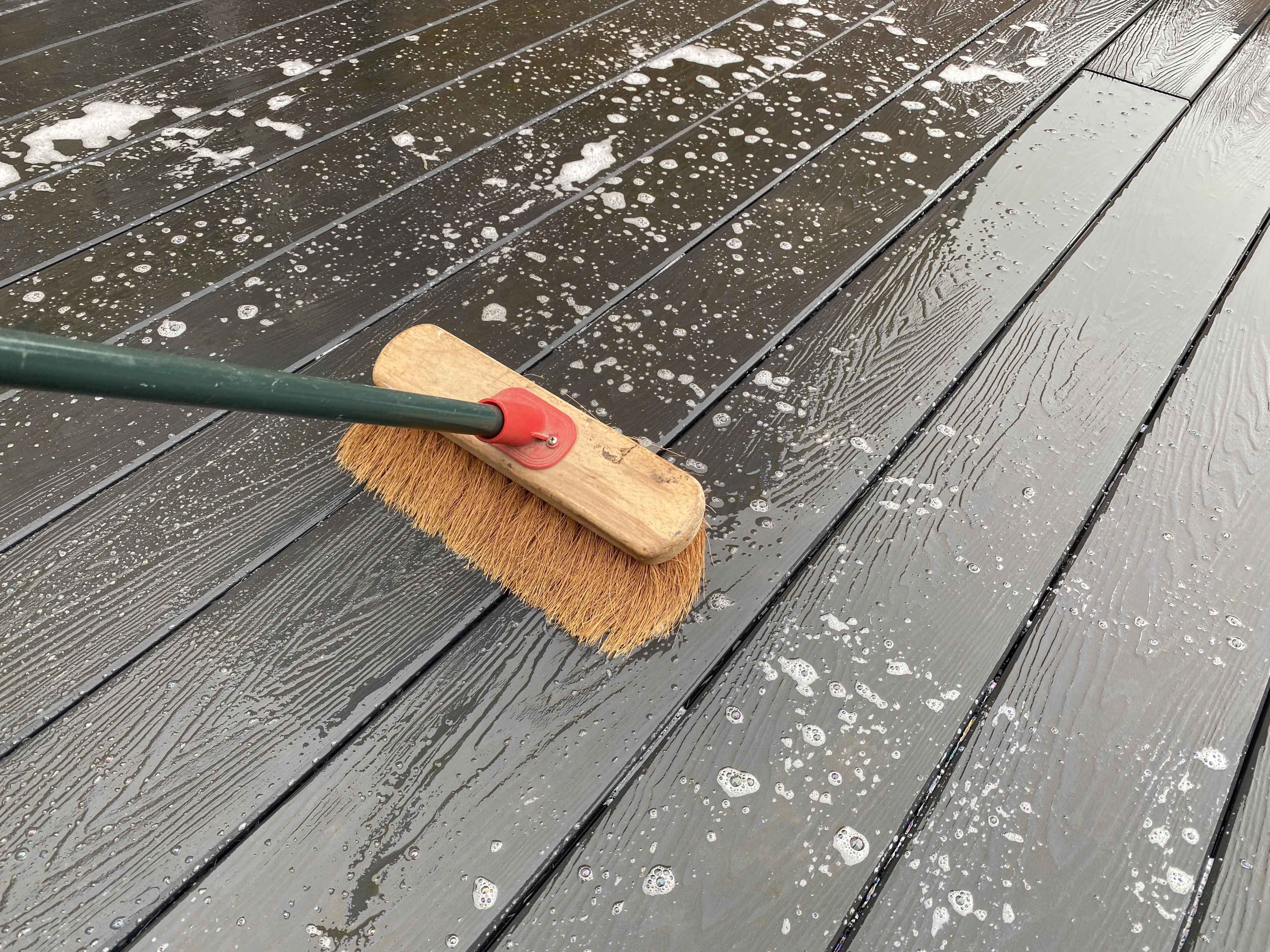 A brush being used with soap and water to scrub down some composite decking to clean it.