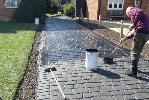 an image of a man using brush to clean the block paving on driveway