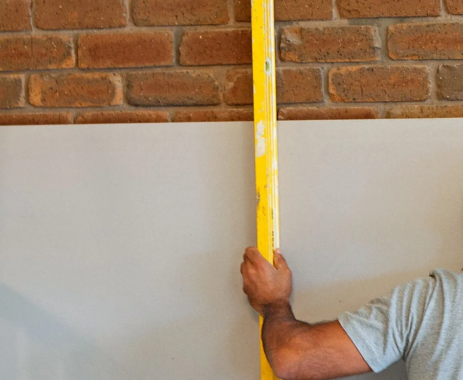 A person using battens to attach plasterboard to a bricked wall.