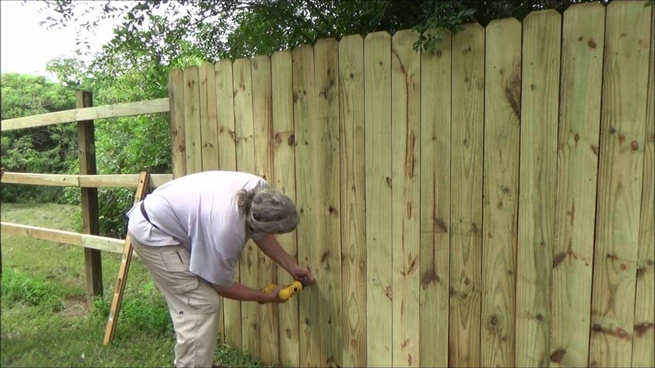 an image of a person using a drill to insert nails into a large, beige coloured fence