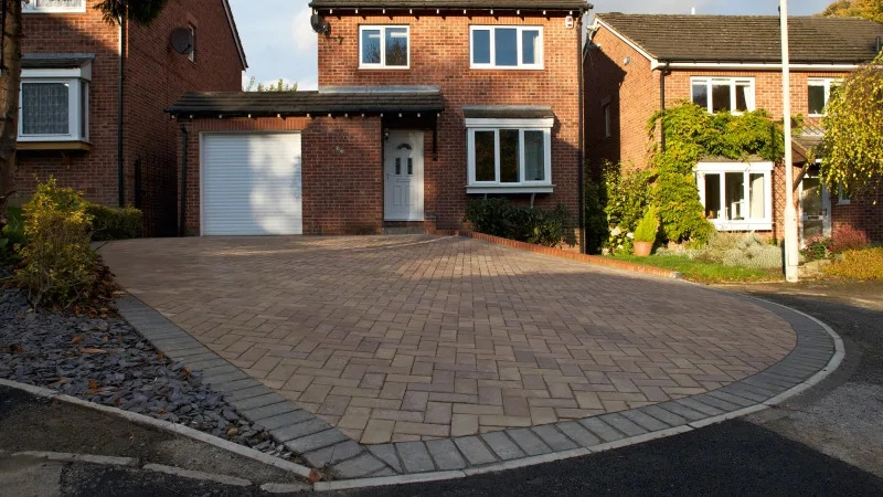 A Marshalls driveway with block paving and houses centered in te background.