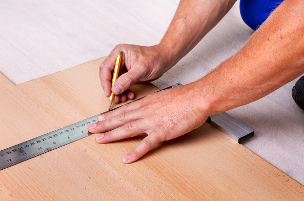 an image of a man using a pencil to measure laminate flooring