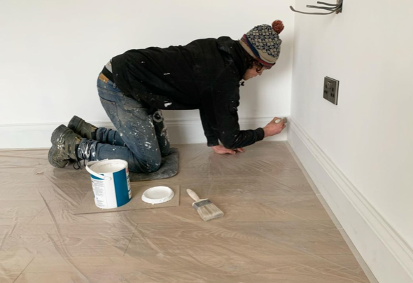 an image of a man painting skirting boards in home