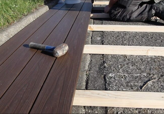 An image of a hammer left on some composite decking whilst someone lays it on top of some wooden joists above some gravel.