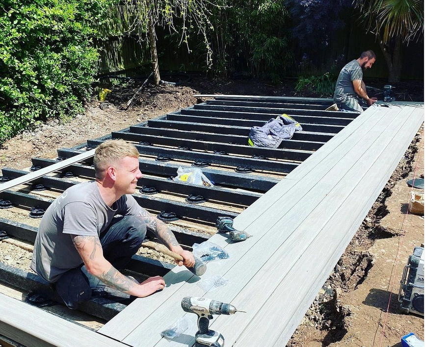 An image showing two men beginning to lay composite decking in a garden.