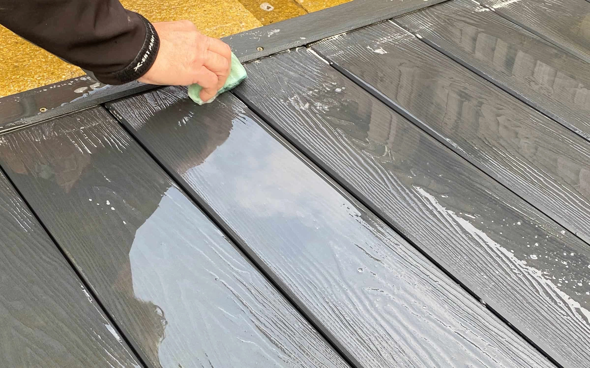 An image of a person using a cloth and water to initially clean their composite decking so it's sparkling queen.