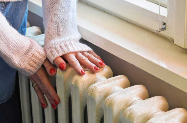 an image of a woman checking the radiator for cold spots with hands