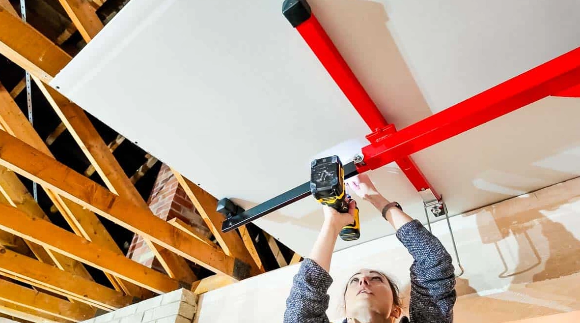 A woman using a drill to attach plasterboard to the ceiling, which we also have a blog on on the site.