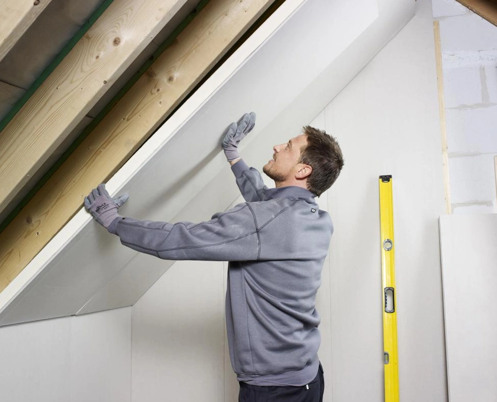A man using gloves hands to attach plasterboard to wall.