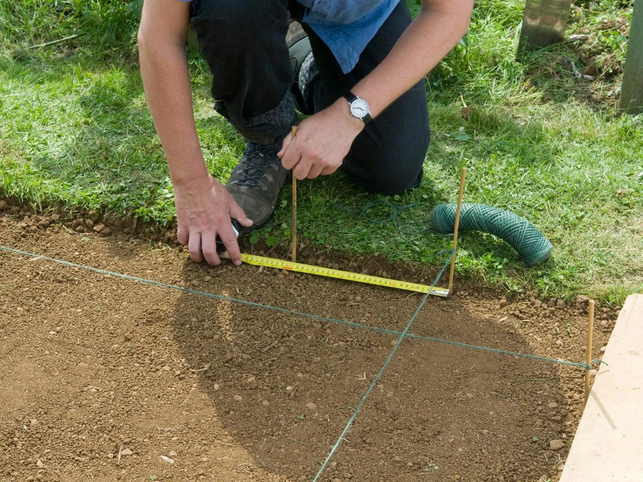 A person using pegs and a measuring tape to mease the 150mm needed to fit a patio above the sub base.