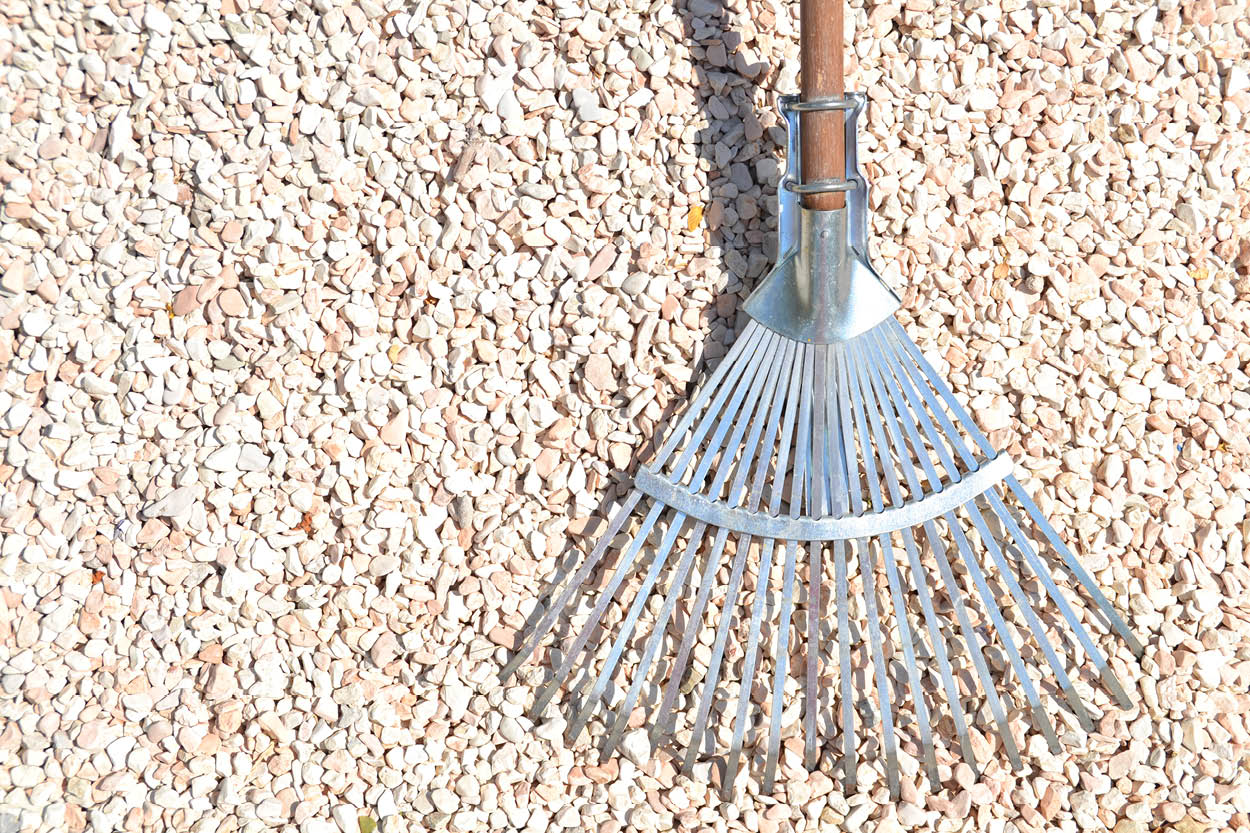 An image showing a rake laid flat on a aggregate surface. This is a tool used for preparing your ground for installing artificial grass.